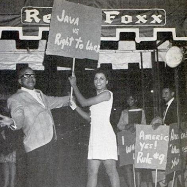 Black and white photo of Sir Lady Java protesting with Red Foxx in front of the Red Foxx Club. Java is holding a sign that reads "Java vs. Right to Work."