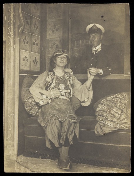 Download the full-sized image of A sailor holds hands with a man in elaborate drag. Photographic postcard, 191-.