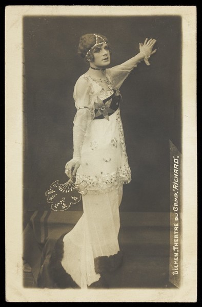 Download the full-sized image of A French prisoner of war acting in an internment camp in Dülmen, performing in drag, wearing a long white dress. Photographic postcard, 191-.