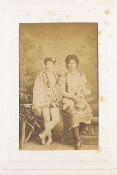 Download the full-sized image of Two men in drag side by side, in front of a painted backrop. Photograph, 189-.