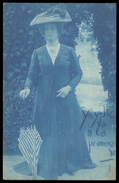Download the full-sized image of An man in drag, wearing a large hat and veil, posing in a garden. Colour process print, 191-.