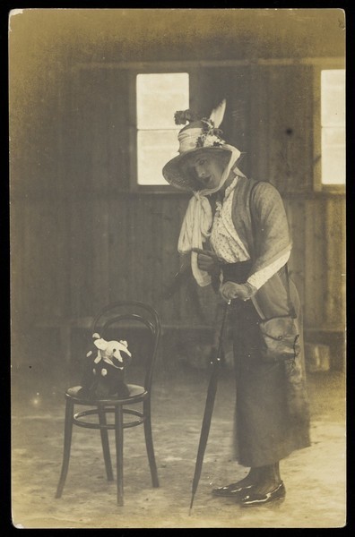 Download the full-sized image of An soldier in drag, dressed in a bonnet and holding an umbrella. Photographic postcard, 191-.