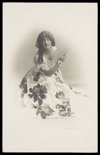 Download the full-sized image of A young man in drag poses in a flowery dress. Photographic postcard, 192-.